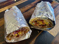 two burritos wrapped in foil on a wooden table